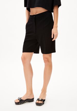 Femme portant un short noir jusqu'aux genoux, un top court noir et des sandales à plateforme noires avec des boucles argentées.