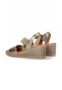 Sandalias de cuña con un empeine metálico bronce, una correa texturizada en beige y una suela de yute trenzado. Diseño de punta abierta con detalles de tiras cruzadas.