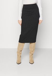 Zwarte midi-rok met tekstpatroon, hoge taille, rekbare stof, gedragen met beige suède laarzen tot boven de dijen, puntige neuzen.