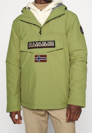 Homme portant une veste Napapijri vert clair avec poche avant à rabat, écusson du drapeau norvégien et pantalon beige, montré du cou aux hanches.