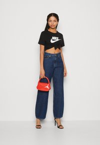 Zwart cropped t-shirt met wit Nike-logo, hooggewijde blauwe denim wide-leg jeans, rode handtas en zwarte stilettohakken.