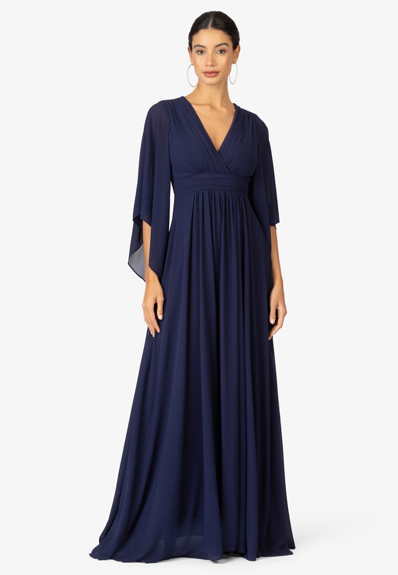 Abito lungo blu navy con scollatura a V, corpino plissettato e maniche a mantello fluide realizzate in un tessuto leggero.