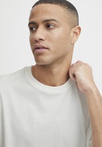 Short-sleeve, crew-neck t-shirt in light cream color, made from soft cotton. The fabric has a smooth texture with minimal seams.