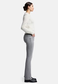 Lys grå slim fit jeans med en frynset kant, parret med en hvid, langærmet sweater. Outten suppleres med sorte sko.