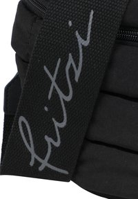 Bolsa de tela negra con una correa texturizada que presenta una firma impresa en gris, cierre con cremallera y secciones blandas y acolchonadas.