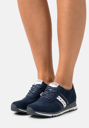 Sneakers in suede blu navy con dettagli bianchi, punta rotonda, lavorazione perforata e suola nera a contrasto. I lacci sono bianchi con una sfumatura di grigio.
