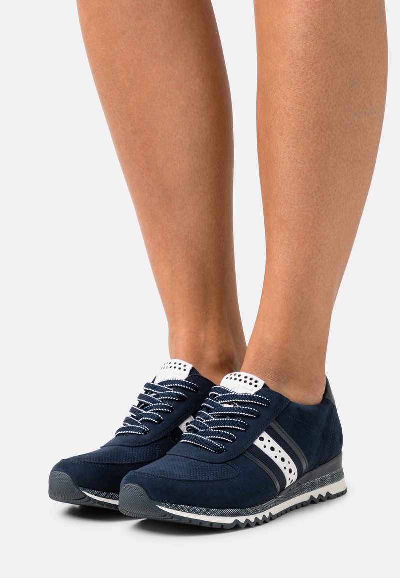 Sneakers in suede blu navy con dettagli bianchi, punta rotonda, lavorazione perforata e suola nera a contrasto. I lacci sono bianchi con una sfumatura di grigio.