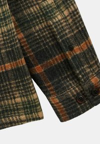 Manches de chemise en flanelle de laine avec un motif plaid vert, marron et orange ; comporte deux boutons foncés et une finition texturée.