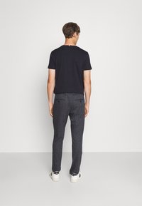 Maglietta nera a maniche corte abbinata a pantaloni slim-fit grigio scuro e sneakers bianche. La maglietta presenta un piccolo accento colorato sul retro.