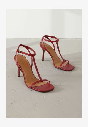 Rode leren sandalen met hoge hakken, voorzien van een T-bandontwerp, vierkante neus en smalle enkelband, met een tan binnenzool en een zwarte buitenzool.