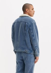 Denim jacket in light blue with a white shearling collar. The fabric has a textured finish and features a button closure and side pockets.