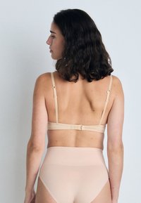 Nude fabric bra with slim straps and adjustable hooks; paired with high-waisted nude panties, smooth texture and seamless design.
