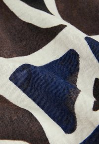 Strukturierter Stoff mit einem Muster aus großen, abstrakten Formen in Dunkelbraun, Dunkelblau und Cremefarben, das ein weiches, gewebtes Material präsentiert.