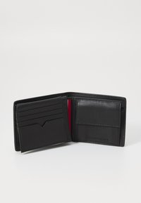 Portefeuille en cuir noir avec six emplacements pour cartes, doublure rouge et un petit compartiment pour des cartes ou des espèces supplémentaires. Présente un logo en relief.