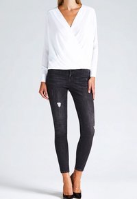 Top bianco annodato con maniche lunghe abbinato a jeans skinny scuri con dettagli strappati e scarpe nere con tacco alto.