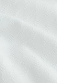 Tissu blanc à motif subtil de losanges et points répétés, présenté avec de douces plis et une texture douce.