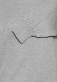 Pikad varrukad ribikättega ja õrna kogumise detailiga heledast hallist kudumist.