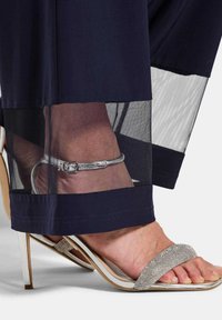 Navy kledingstuk met doorzichtige mesh zoom, met een zilveren enkelband sandaal met een glinsterende band en een naaldhak.