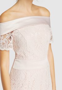 Verkkopuku, jossa on olkapäiltä avonainen satiinikaulus, lyhyet verkkohihat, vaaleanpunainen väri, kapea vartalo ja satiinivyötärö.