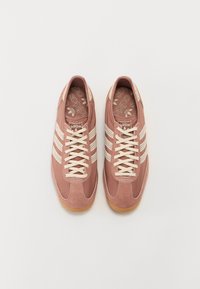 Pair of dusty pink Adidas sneakers with white stripes and laces, viewed from above on a plain white background.