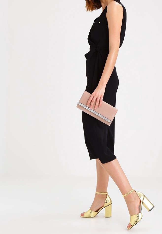 Abito senza maniche nero con un dettaglio legato in vita, abbinato a una pochette rosa con un accento argentato e sandali con tacco quadrato dorato.