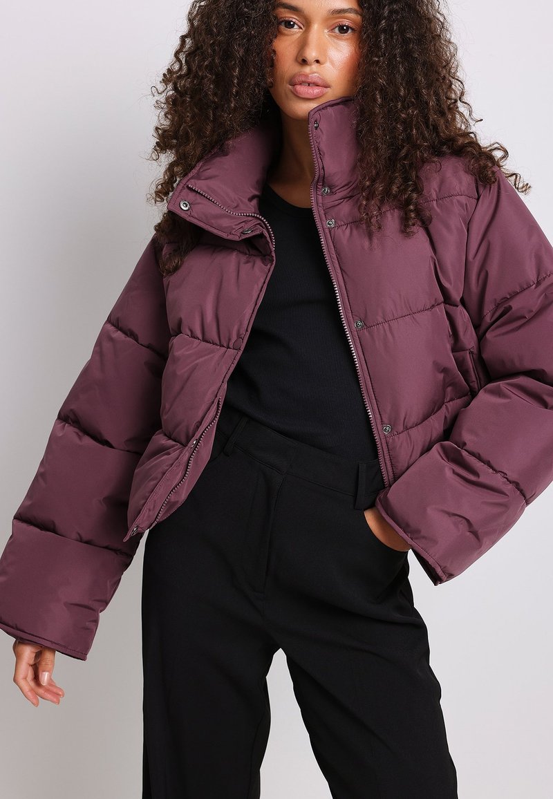 Trumpas violetinis pūkų džemperis su aukšta apykakle, užsegamas užtrauktuku ir spaudėmis, išsiplėtusiais rankovėmis ir lygia, blizgia tekstūra.