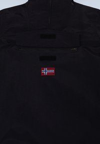 Giacca blu navy con tasca con zip e dettagli in Velcro. Applicazione ricamata con bandiera norvegese sopra la tasca. Tessuto dalla texture liscia.