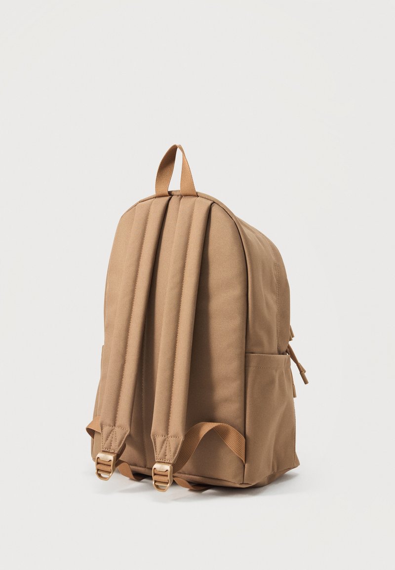 Zaino in tessuto color cognac con spallacci imbottiti regolabili e tasche laterali, visto da dietro su sfondo bianco neutro.