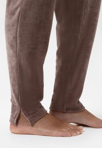 Fluwelen loungebroeken in een gedempt bruine kleur, met een relaxte pasvorm en enkelopeningen voor extra comfort, en een gladde, zachte textuur.