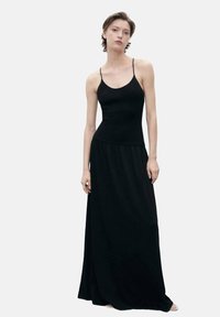 Black maxi dress with thin spaghetti straps, fitted bodice, and a flowing skirt. Made of soft, draping fabric with a smooth texture.