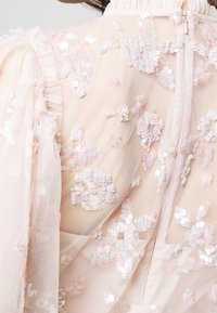 Vêtement rose pâle transparent orné de sequins irisés et de manches en tulle volanté, avec un col montant et une fermeture éclair à l'arrière.
