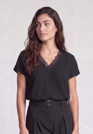 Young woman with long wavy hair wearing a black lace-trimmed V-neck blouse and black high-waisted pants with a belt.