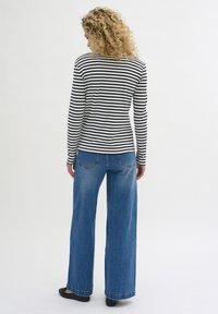 Striped long-sleeve shirt in black and white, paired with blue wide-leg jeans. The top fits snugly, while the jeans have a relaxed silhouette.