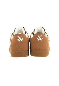 Chaussures en suede marron avec une texture lisse et un logo blanc sur le talon. Présentent un collier rembourré et une doublure de couleur claire en contraste.