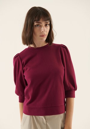 Pull en bourgogne avec des manches courtes bouffantes, texture tricotée, col rond et ourlet ajusté, conçu pour un ajustement décontracté.