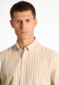 Beige en witte gestreepte shirt met een button-down kraag, met een textuurstof en zichtbare knopen aan de voorkant.