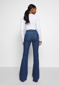 Högmidjade utsvängda jeans i mörkblå denim med kontrasterande sömmar, femfickorsdesign och subtil slitna detaljer vid bakfickorna.