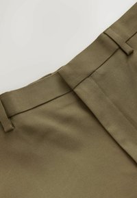 Vihreät oliivinväriset housut, joissa on sileä rakenne, litteä vyötärö, vyölenkit ja yksi taitos edessä.