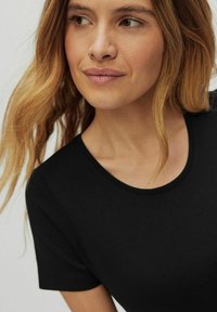 Czarna koszulka z krótkim rękawem o okrągłym dekolcie, gładkiej fakturze i dopasowanym kroju. Materiał wydaje się miękki i lekki.