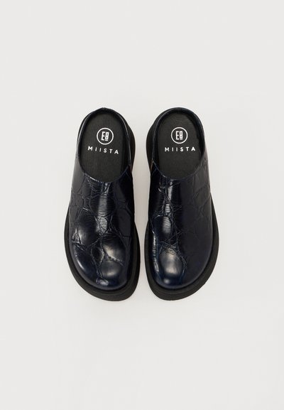 Saboti din piele de culoare bleumarin, cu o suprafață texturată, vârf rotund și o talpă joasă de culoare neagră. Au un design ușor de încălțat și un logo pe interior.
