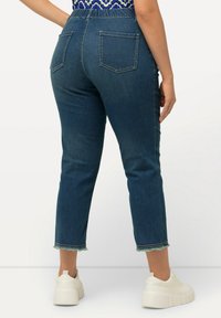 Tmavě modré džíny s vysokým pasem, mají zadní kapsy a roztrhaný lem. Sluší jim objemné bílé tenisky.