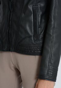 Schwarze Lederjacke mit Paneeldetails, Reißverschluss vorne und gerippten Akzenten an den Ärmelbündchen. Verfügt über seitliche Taschen zur Aufbewahrung. Strukturiertes Finish.