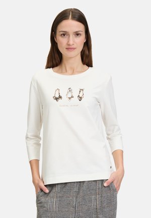 Langærmet hvid t-shirt med en glat tekstur, prydet med et grafisk print af sko og teksten "bella vita" i bløde farver.