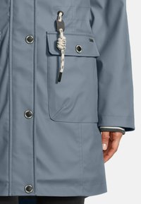 Gray raincoat with large front pocket, black snap buttons labeled "New View," and white rope drawstring, worn over layered sleeves.