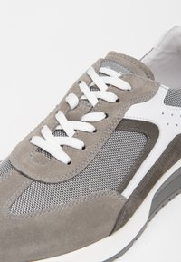 Sneaker grigia in suede e mesh con dettagli bianchi, lacci rotondi e una suola testurizzata dal design elegante.