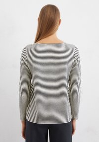 Striped long-sleeve top in cream and black, featuring a round neckline and a relaxed fit. Soft fabric with a slightly textured finish.
