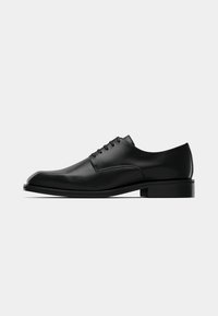 Chaussure Oxford en cuir noir avec un bout pointu et élégant, une texture lisse et des coutures minimalistes. Elle présente un talon carré bas et un design à lacets.