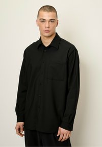 Chemise à manches longues noire avec boutonnière, dot�ée d'une poche poitrine, fabriquée en tissu texturé, avec un col classique et des poignets boutonnés.
