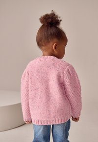 Cardigan rosa lavorato a maglia con motivo strutturato, scollo rotondo, orlo a coste e maniche gonfie, abbinato a jeans di denim blu.