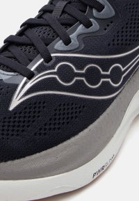 Κοντινή λήψη μαύρου και γκρι παπουτσιού τρεξίματος με επάνω μέρος από δίχτυ, μαύρα κορδόνια, λογότυπο με κυματιστή μορφή και λευκή σόλα με την ένδειξη «PWRRUN+».